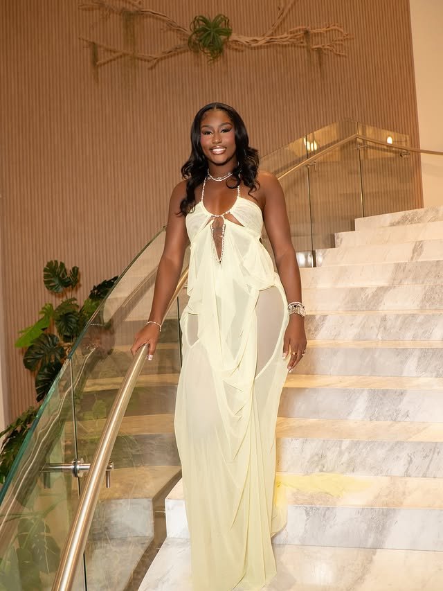 Alycia Parks in a flowing pale yellow gown descending a marble staircase, hand on the rail